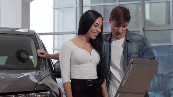 Glückliches junges Paar kauft neues Auto im Autohaus, liest Infopapier — Stockfoto