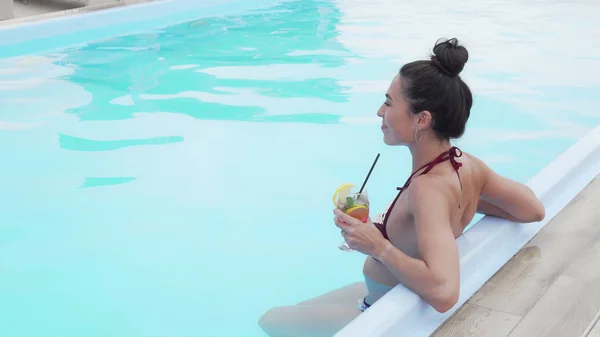 Visão traseira tiro de uma mulher linda bebendo coquetel em uma piscina — Fotografia de Stock