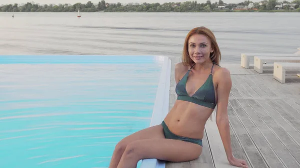 Gyönyörű nő egy bikini mellett ülve a medence a strandon — Stock Fotó