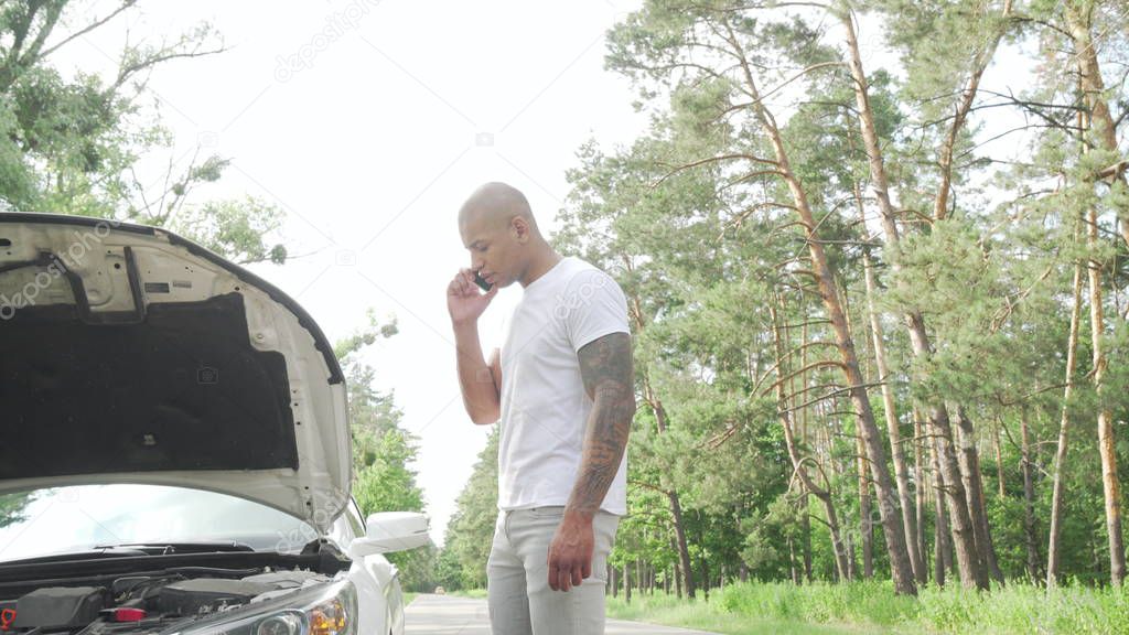 Handsome African man calling tow truck service on countryside road
