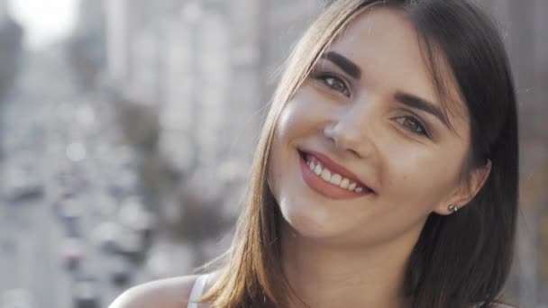 Lovely young happy woman smiling to the camera with city streets on background — Stock Video