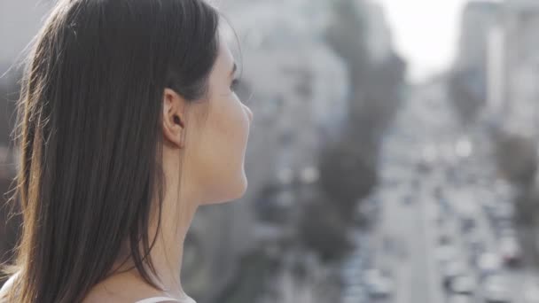 Молодая женщина улыбается в камеру через плечо, наблюдая оживленный город — стоковое видео