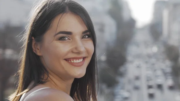 Jovem mulher sorrindo para a câmera sobre o ombro enquanto observa a cidade ocupada — Fotografia de Stock