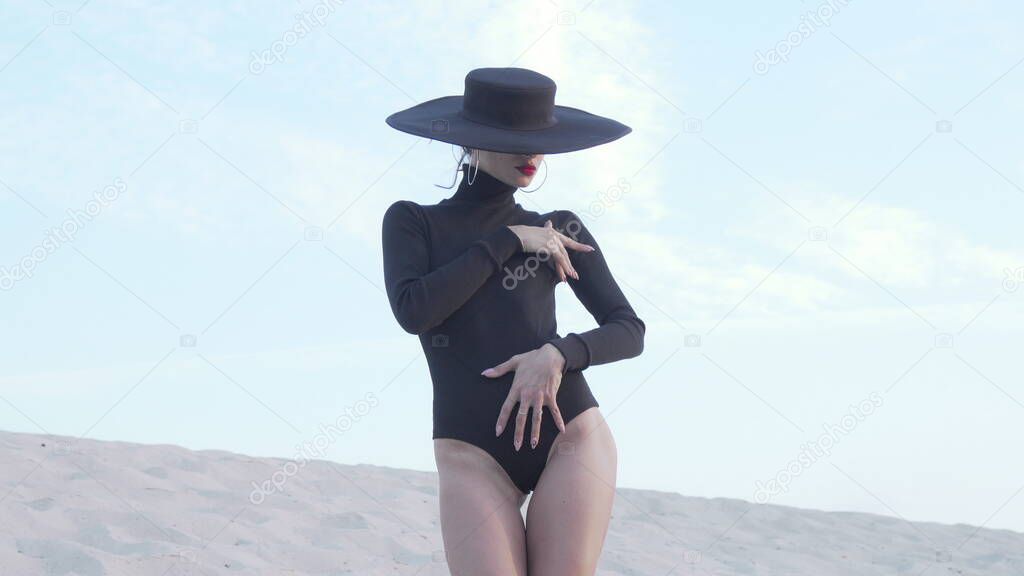 Gorgeous woman in black bodysuit and hat posing gracefully outdoors