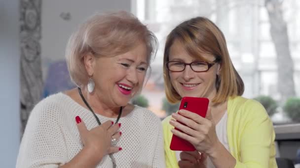 Mujer madura mostrando algo en su teléfono inteligente a su madre mayor — Vídeo de stock