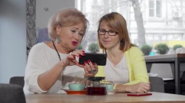 Olgun kadın ve kıdemli annesi kafede birlikte akıllı telefon kullanıyorlar.