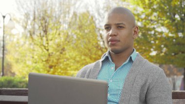 Sonbaharda yerel parkta dizüstü bilgisayarda çalışan Afrikalı Amerikalı bir adam.
