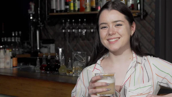 Atrakcyjna młoda kobieta uśmiechnięta do kamery podczas picia koktajlu w barze — Zdjęcie stockowe