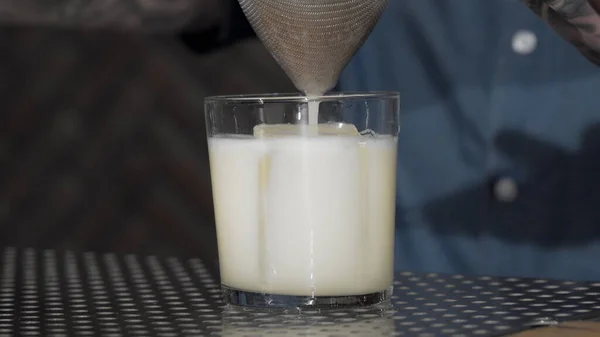 Cocktail sendo derramado no copo sobre cubo de gelo — Fotografia de Stock