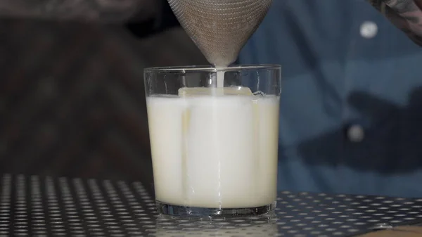 Cocktail being poured into the glass over cube of ice — Stock Photo, Image