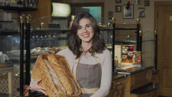 신선 한 빵이 담긴 바구니를 들고 카메라 앞에 미소짓는 행복 한 여성 제빵사 — 스톡 사진