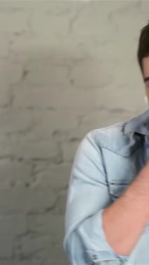 Şık kot gömlekli çekici bir genç adam aynanın önünde şakacı bir şekilde poz veriyor, yüzünde tıraş köpüğünün dokunuşunu gösteriyor. Kendine güveni ve gevşek tavırları dokulu gri tuğla zemine karşı davetkar bir atmosfer yaratıyor.