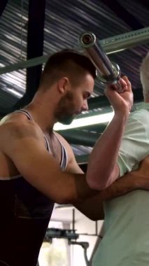 Kararlı bir son sınıf öğrencisi spor salonunda halterle güçlü bir şekilde çömeliyor. Kuvveti ve direnci somutlaştırıyor. Destekleyici, genç, sakallı bir antrenör arkasında duruyor. Nesiller boyunca akıl hocalığı ve takım çalışmasının ilham verici bağını gösteriyor.