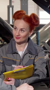 Canlı kızıl saçlı yetenekli bir bayan tamirci ve erkek arkadaşı otomotiv dünyasında ekip çalışmasını özenle inceliyor. Şık gri üniformalı kadın, parlak sarı bir panoya titiz notlar alır.