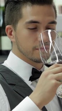 Zarif papyonlu şık genç bir adam şarap şişelerinin zarif bir gösterisiyle çevrili bir bardak koyu kırmızı şarabın tadını çıkarırken gözlerini mutlulukla kapatır. Özgüvenli tavrı sofistike ve uzmanlık yayıyor, sizi lüks şeyleri keşfetmeye davet ediyor.