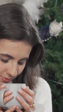 Neşeli bir kadın, güzel süslenmiş bir Noel ağacının zemininde sıcaklıkla parlayan huzurlu gülüşü, tüten bir fincan çayı nazikçe beşiğine yatırır. Bu büyüleyici sahne, tatil neşesinin özünü yakalar, izleyicileri sıcacık kucaklamaya davet eder.