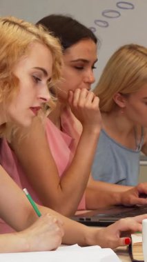 Canlı bir sahnede, üniversite konferans salonundaki bir projede tutkuyla işbirliği yapan çarpıcı bir kız öğrencinin de aralarında yer aldığı çeşitli bir grup öğrenci notlar sergileniyor. Bu dinamik atmosfer kararlılık ve takım çalışması yayar.