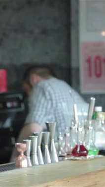 Gündelik tişörtlü, modaya uygun sarışın bir adam hareketli bir barda soğuk bira ısmarlamak için el kol hareketi yapıyor. Canlı atmosfer renkli şişeler ve misafirperver bir barmenle gelişir. Bu da onu sosyalleşme ve eğlenme için ideal bir yer yapar.