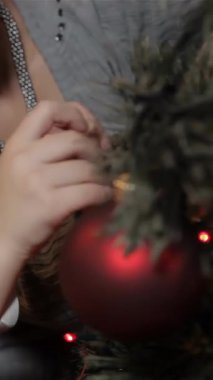 Neşeli esmer bir kadın ve sevimli küçük bir kız, canlı kırmızı bir süsü verimli bir Noel ağacına nazikçe asarlarken yürek ısıtan bir anı paylaşıyorlar. Işıl ışıl gülüşleri ve ışıl ışıl gözleri samimi odayı aydınlatıyor ve büyülü bir ışık yaratıyor.