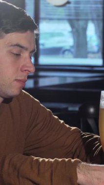 Sıcak bir gülümsemesi olan neşeli genç bir adam soğuk bir bardak bira tutuyor, yumuşak akşam ışığıyla dolu sıcak bir barda neşe saçıyor. Çevrenin nazik parıltısıyla vurgulanan davetkar atmosfer rahatlamak için mükemmel bir sahne hazırlıyor.