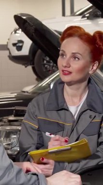 Neşeli kıvırcık saçları olan çekici bir bayan tamirci, hareketli bir garajda iş arkadaşıyla araba tamirini tartışırken hevesle notlar alır. Bu canlı sahne takım çalışmasının dinamik enerjisini yakalar.