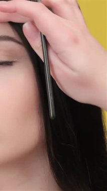 Yetenekli bir vize uzmanı güzel bir Asyalı kadının saçını nazikçe tutar ve onu titizlikle göz makyajı uygulamasına hazırlar. Parlak sarı arka plan enerji yayıyor. Modelleri, dingin ifadesini ve sanatsal özelliklerini vurguluyor.