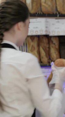 Gıcır gıcır beyaz bir gömlek ve önlükle giyinmiş neşeli genç bir fırıncı, samimi bir kahve dükkanında sıcak, altın bir somun ekmek sunar. Davetkar atmosfer, yeni pişmiş hamur işlerinin enfes kokusuyla zenginleşir ve müşterileri cezbeder.