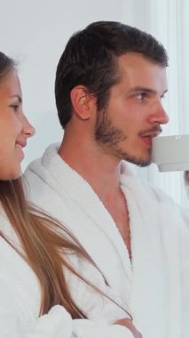 Pofuduk beyaz bornozlara sarılı neşeli bir çift, pencerenin kenarında birbirlerine sevgiyle bakıyor, kahkahaları otelin süitinde yankılanıyor. Güneş ışığı perdelerin arasından akar, şefkatli gülümsemelerinin üzerine sıcak bir parıltı saçar,