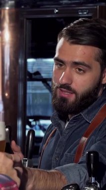 Karizmatik sakallı bir barmen, kadife gibi koyu bir biradan zevk alır, müşterisiyle içli dışlı olur, o da kutlama kadehinde neşeyle köpüklü bir bardak kaldırır. Bu canlı bar sahnesi yoldaşlık ve şenlik ruhunu yansıtıyor.