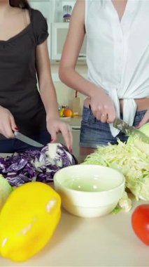 Renkli sebzelerle dolu canlı bir mutfakta, iki genç kadın hevesle taze malzemeleri doğruyor, enfes bir mutfak karışıklığı yaratıyorlar. Parlak gülüşleri ve neşeli enerjileri yemek pişirme sanatında birleşirken havayı neşeyle dolduruyor.