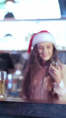 Şenlikli süslemelerle süslenmiş hareketli bir barda, Noel Baba şapkalı iki arkadaş coşkuyla bira bardaklarını kaldırarak tatil ruhunu kutluyorlar. Arka planda neşeli barmen ışıkları, kahkahalarla dolu canlı atmosferi güçlendiriyor.