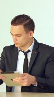 Gösterişli bir modern ofiste, özel dikim takım elbiseli odaklanmış genç bir işadamı bir elinde bir telefon görüşmesi yaparken bir tablet tutuyor, profesyonellik ve hırs yayıyor. Parlak, minimalist çalışma alanı onun gibi üretkenlik atmosferini arttırır.