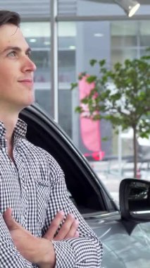 Parlak bir gülümsemesi olan cesur genç bir adam canlı bir galeride şık, modern bir arabaya yaslanıyor. Neşeli ifadesi, parlak araçlar ve parlak, davetkar bir sergi salonu atmosferiyle çevrili potansiyel sahipliğin heyecanını yakalıyor.