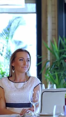 Yumuşak mum ışığıyla süslenmiş rahat bir restoranda, zarif bir masada oturan güzel bir kadını selamlayan, onu nazikçe öpen ve kolunu omzuna dolayan çekici bir adam. Bu samimi an sevgi ve neşe saçıyor.