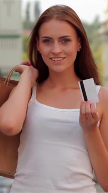 Şık, genç bir kadın, hareketli bir şehir caddesinde neşeyle ışıldıyor, bir elinde alışveriş çantalarını, diğer elinde kredi kartını zahmetsizce sergiliyor. Onun ışıl ışıl gülüşü ve şık kıyafeti şehir alışveriş maceralarının heyecanını yakalıyor.