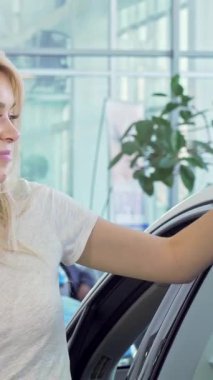 Parlak, havadar bir galeride lüks, modern bir otomobilin yanında arabasının anahtarlarını tutarken neşe saçan parlak sarı saçlı genç bir kadın. Bu canlı sahne, onun bulaşıcı gülümsemesini vurgulayarak, yeni mülkiyetin heyecanını yakalıyor.