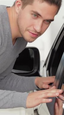 Şık bir genç adam, modern bir sergi salonunda yeni arabasının şaşaalı kapanışından büyülenmiş, pırıl pırıl bir gülümseme ile öne eğilir. Bu canlı sahne heyecan ve memnuniyet saçıyor, müşteri ve otomotiv arasındaki neşeli bağlantıyı vurguluyor.