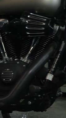 Şık sakallı, genç, beyaz bir adam parlak bir motosiklet atölyesinin parlak zemininde, akıllı telefonuyla mesajlaşmak için öylesine oturuyor. Parlak krom ve güçlü motorlarla çevrelenmiş halde, motosikletçiliğin füzyonunu mükemmel bir şekilde yakalıyor.