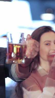 Genç yetişkinlerden oluşan canlı bir üçlü, iki kadın ve bir erkek, canlı bir barda arkadaşlıklarını kutlamak için soğuk bardaklarla coşkuyla tezahürat yapıyorlar. Işıltılı gülümsemeleri ve coşkulu jestleri arkadaşlığın heyecanını özetliyor.