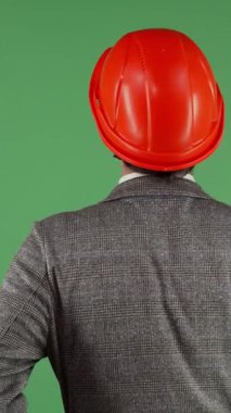 A focused male contractor in a striking red hardhat stands with his back to the viewer, surveying a vibrant green chromakey backdrop. This dynamic image captures the essence of innovation and professionalism in construction, blending creativity with