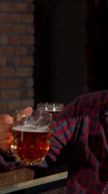 A mature bearded man takes a hearty sip of frothy beer, fully immersed in a lively conversation with his friend at a cozy pub. The rustic brick walls and warm lighting create an inviting atmosphere, perfect for celebrating friendship and shared