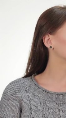 A joyful brunette girl with long, flowing hair playfully signals for silence, her finger pressed to her lips against a soft, luminous white backdrop. This enchanting portrait exudes charm and positivity, capturing her youthful spirit and inviting