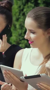 Three dynamic businesswomen stand outside a sleek office, animatedly discussing their impressive results while reviewing a tablet. Their radiant smiles and chic outfits radiate an atmosphere of empowerment and teamwork against a backdrop of lush