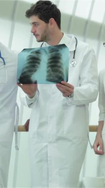 Three dedicated doctors, including a woman with red hair and glasses, a man in a crisp white coat, and another in a sharp suit, intently examine a lung X-ray, shedding light on the perils of smoking. Their serious expressions and professional attire