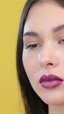 In this captivating close-up, a skilled visagist artfully applies eyeliner to accentuate the striking features of a beautiful Asian model. The vibrant yellow backdrop radiates energy, emphasizing the meticulous artistry and precision that defines the