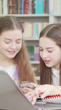 A dedicated teen schoolgirl is deeply engaged in her assignment, surrounded by friends in a vibrant library brimming with colorful books. The lively atmosphere buzzes with teamwork and camaraderie as they collaborate on their studies, embodying the