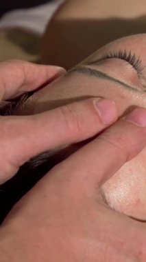 A mature woman relaxes deeply as skilled hands gently massage her head and face, enveloping her in tranquility. The soft, ambient lighting and soothing aromas create a peaceful sanctuary, enhancing her wellness journey and inviting pure bliss