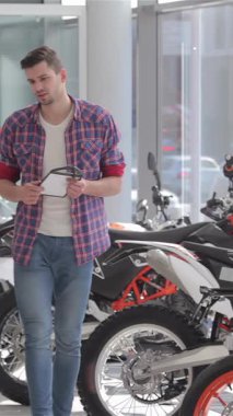 In a lively motorbike salon, a confident seller and an enthusiastic customer engage in a firm handshake, sealing their exciting deal. Surrounded by a dazzling array of sleek cross motorbikes, the bright showroom buzzes with energy, reflecting the