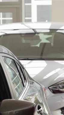 A young man eagerly explores the luxurious interior of a cutting-edge car in a bright, contemporary auto showroom, surrounded by gleaming vehicles. His focused gaze and enthusiastic demeanor reflect the thrill of discovering advanced automotive