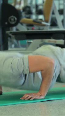 Ortadoğu kökenli kararlı genç bir adam şık, modern bir spor salonunda canlı yeşil bir paspasın üzerinde zorlu bir şınav çekmeyi enerjik bir şekilde bitiriyor. Odaklanmış ifadesi ve iyi tanımlanmış kasları adanmışlık ve güç yayıyor.